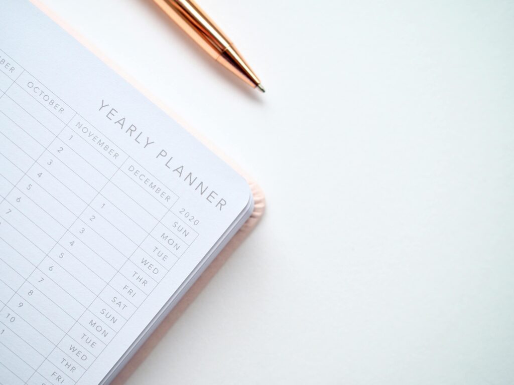 A stylish yearly planner open to a 2020 calendar page, accompanied by a golden pen on a clean white surface.